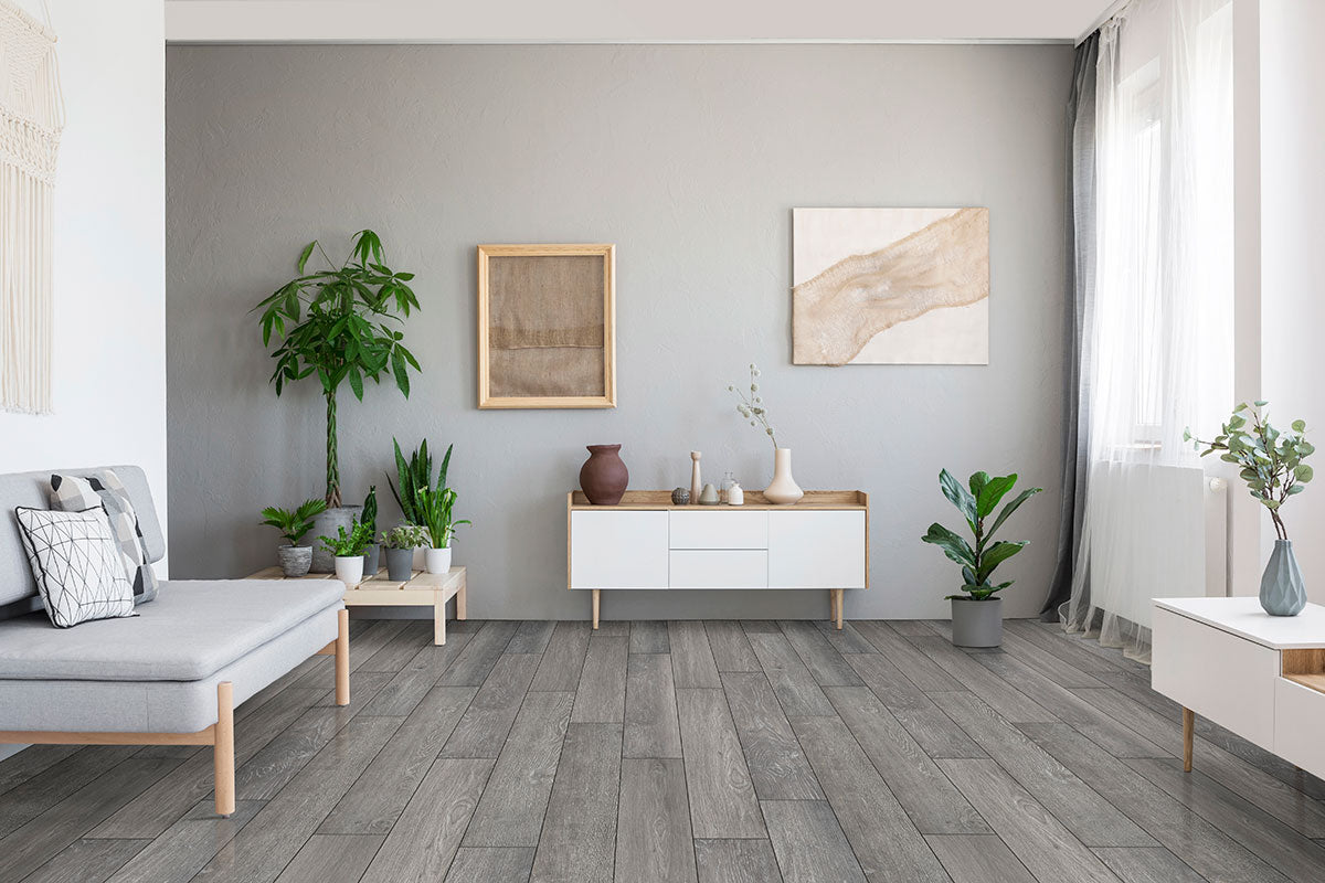 A modern living room features MSI XL Cyrus Finely Luxury Vinyl Planks flooring (22.44 sqft/box), white furniture, potted plants, minimalist art on light gray walls, and sunlight streaming through sheer curtains on a tall window.