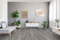 A modern living room features MSI XL Cyrus Finely Luxury Vinyl Planks flooring (22.44 sqft/box), white furniture, potted plants, minimalist art on light gray walls, and sunlight streaming through sheer curtains on a tall window.