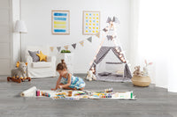 A young girl in a blue dress paints on XL Cyrus Finely Luxury Vinyl Planks by MSI, featuring a CrystaLux Protective Layer, in a bright playroom with a teepee, stuffed animals, art supplies, and playful wall art.