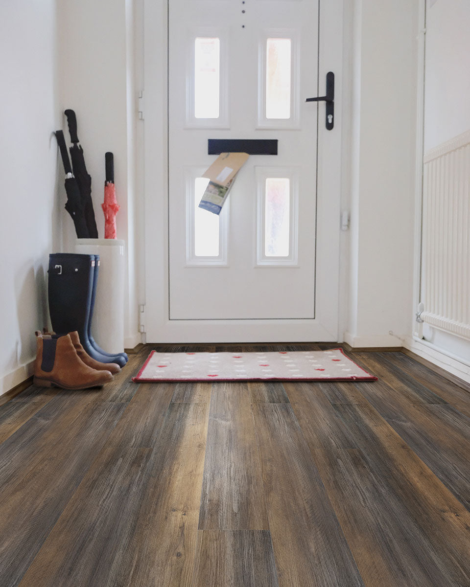 A white front door with a mail slot holding an envelope. The entryway features a red-rimmed doormat, boots, umbrellas, and easy-to-maintain MSI XL Cyrus Hawthorne Luxury Vinyl Planks flooring (22.44 SQFT box).