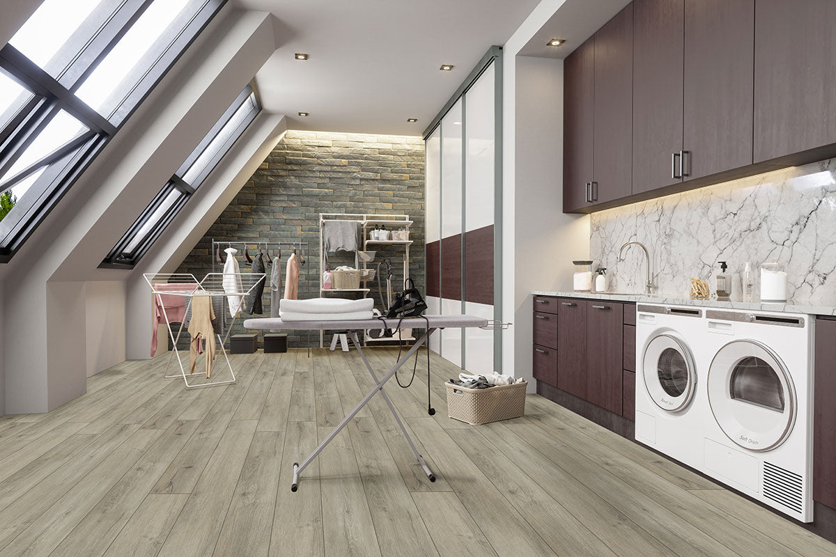 A modern laundry room with slanted windows, dark cabinets, and a marble backsplash—featuring MSI XL Cyrus Kardigan Luxury Vinyl Planks for waterproof, durable flooring—plus washer, dryer, ironing board, drying rack, lounge area, and bathtub.