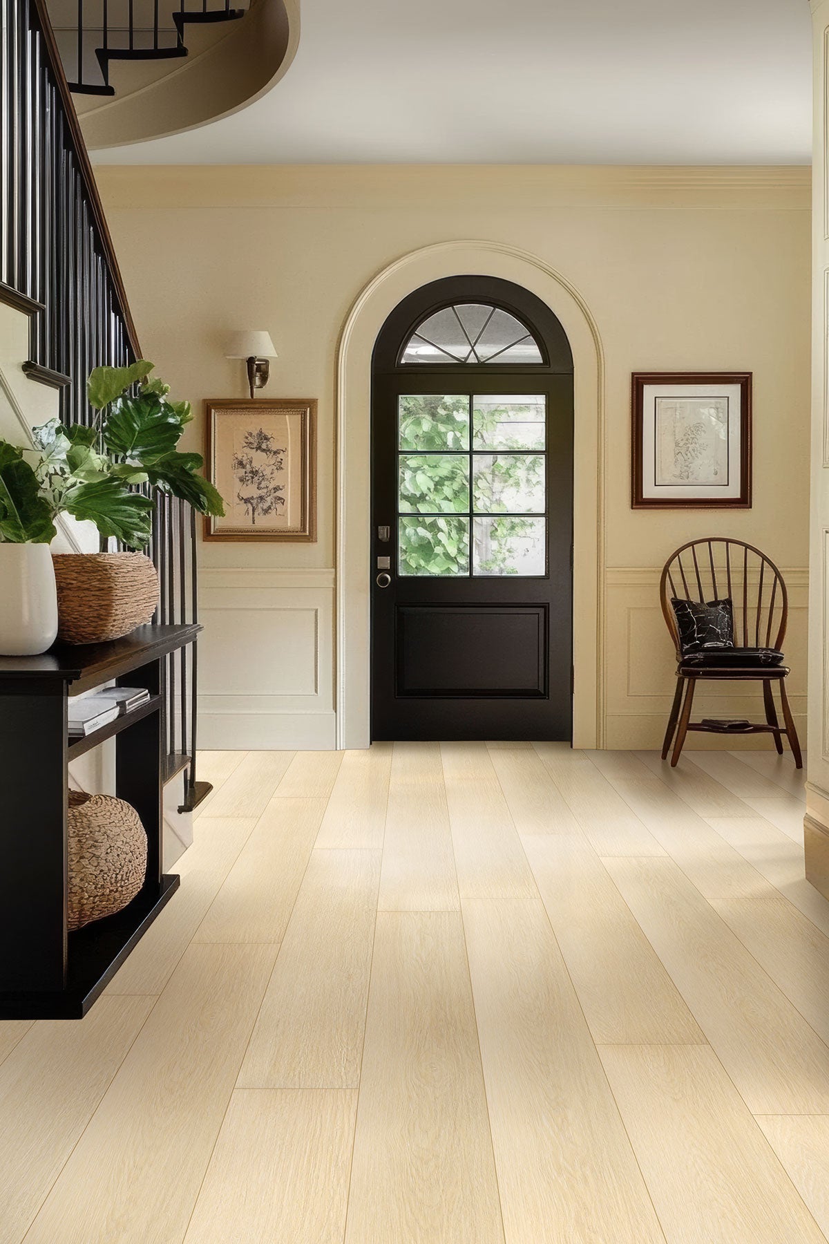 A bright entryway featuring MSI XL Cyrus Lenexa Creek Luxury Vinyl Planks, a black front door with a window, potted plants on a black console table, framed art on cream walls, and a wooden chair near the door.