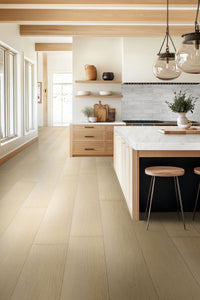 Modern kitchen with light wood floors in MSI XL Cyrus Lenexa Creek Luxury Vinyl Planks, white cabinets, marble island, wood stools, pendant lights, and large windows. Open shelves with pottery and plants create a bright, airy vibe.