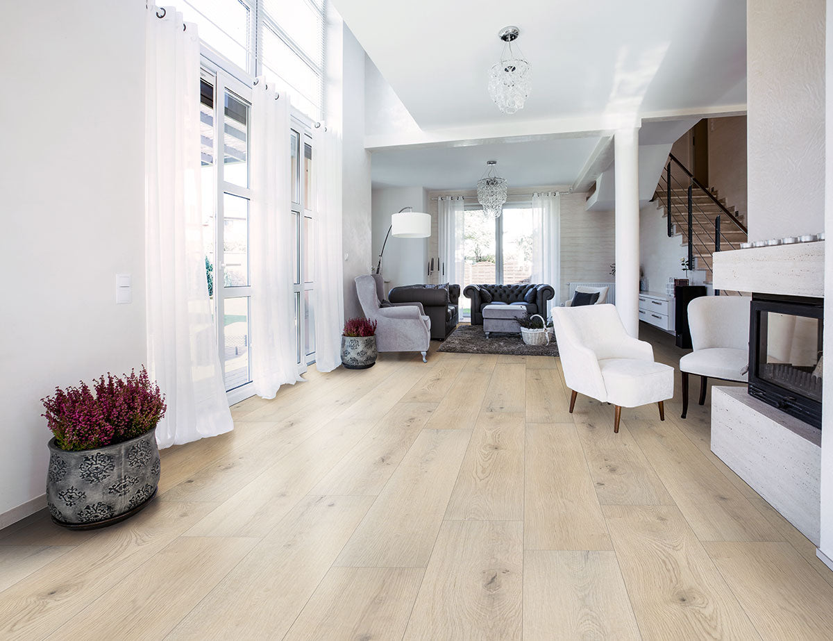 Bright, modern living room with large windows, white walls, elegant furniture, fireplace, and potted plants. Stairs lead up. Floors feature MSI XL Cyrus Runmill Isle Luxury Vinyl Planks for a stylish light wood look and sheer curtains let in natural light.