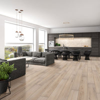 Modern open-plan living room and kitchen with large windows, gray sectional, round coffee table, dark dining chairs, wood floors featuring MSI XL Cyrus Runmill Isle Luxury Vinyl Planks with CrystaLux Protection, potted plants, and sleek dark cabinetry.