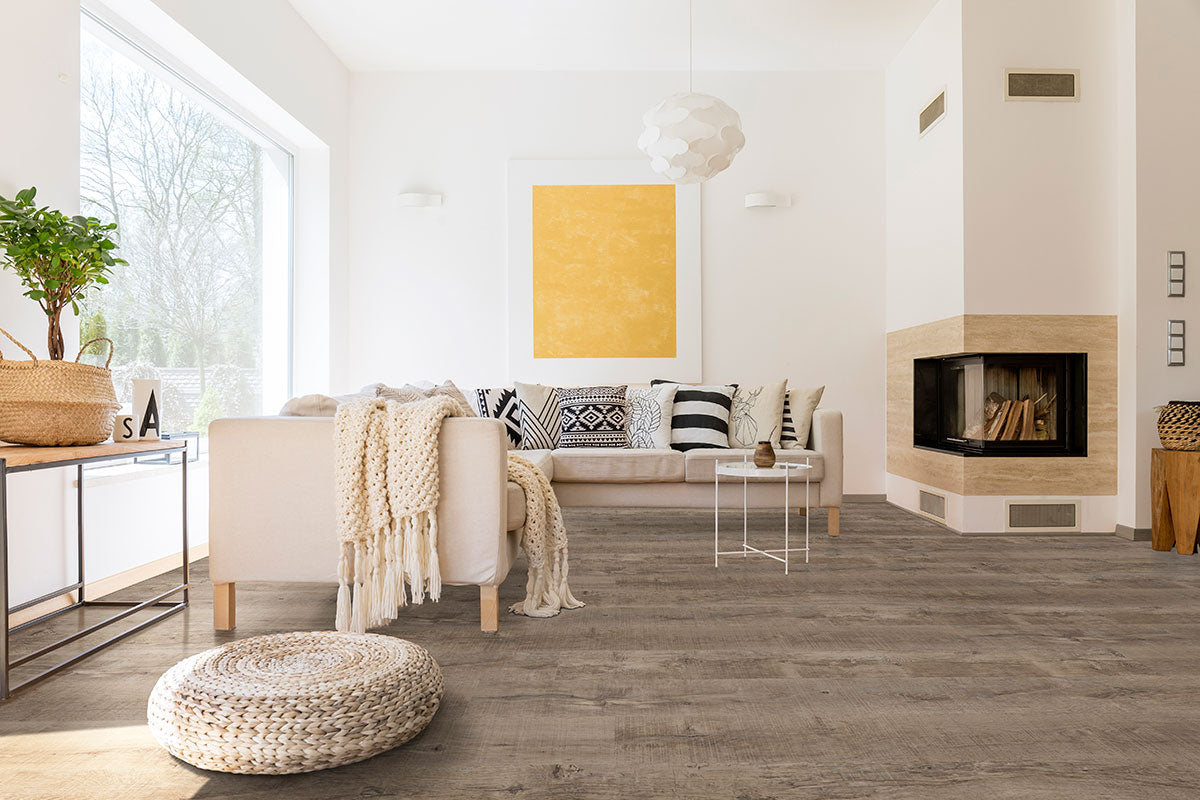 A bright living room with a light sofa, patterned pillows, and modern decor features MSI’s XL Cyrus Ryder Luxury Vinyl Planks BOX (22.44 SQFT) for style and durability, while a large window brings in abundant natural light and warmth.