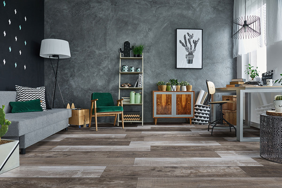 Modern living room with a grey sofa, green armchair, wood furniture, plants, art, lamp, and a desk by the window. The floor is MSI’s XL Cyrus Weathered Brina Luxury Vinyl Planks (22.44 SQFT), featuring an elegant wood-look tile pattern.