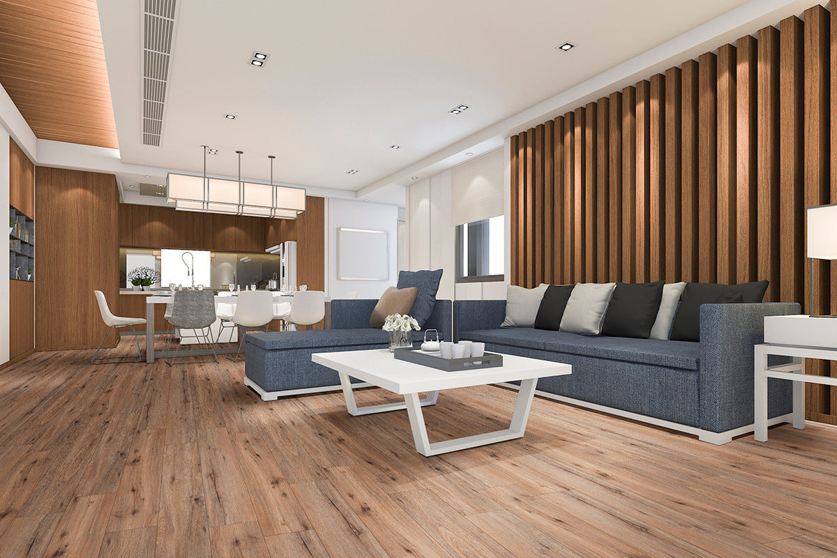 Modern living room with MSI XL Cyrus Fauna Luxury Vinyl Planks flooring, a large gray sectional sofa, cushions, a white coffee table, and wooden slat accent wall. Dining area features white chairs and pendant lighting in the background.