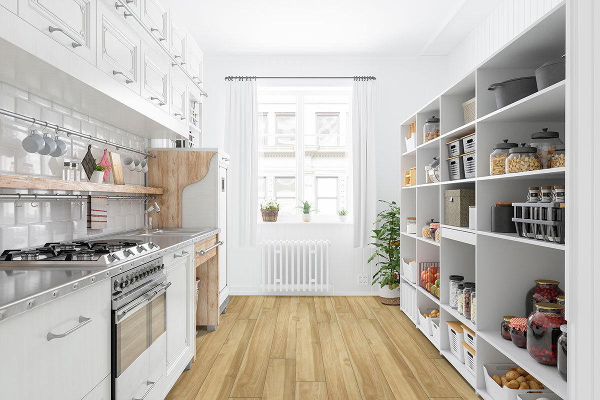 A bright, modern kitchen features white cabinets, open pantry shelves with jars and baskets, stainless steel appliances, sunlit windows, and MSI XL Cyrus Brookline Luxury Vinyl Planks (22.44 SQFT), offering style and durability underfoot with CrystaLux™ protection.