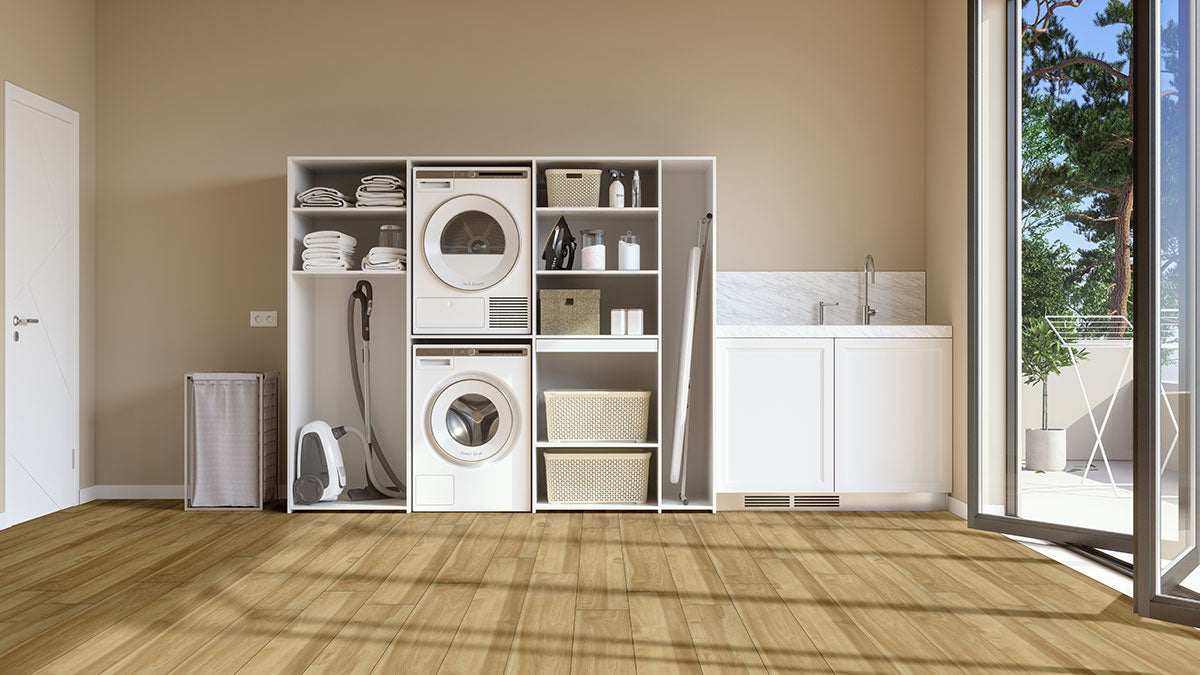 Modern laundry room featuring a washing machine, dryer, shelving for towels and baskets, vacuum, ironing board, white cabinets, sink, and glass doors. MSI XL Cyrus Brookline Luxury Vinyl Planks offer stylish, durable flooring with CrystaLux™ protection.