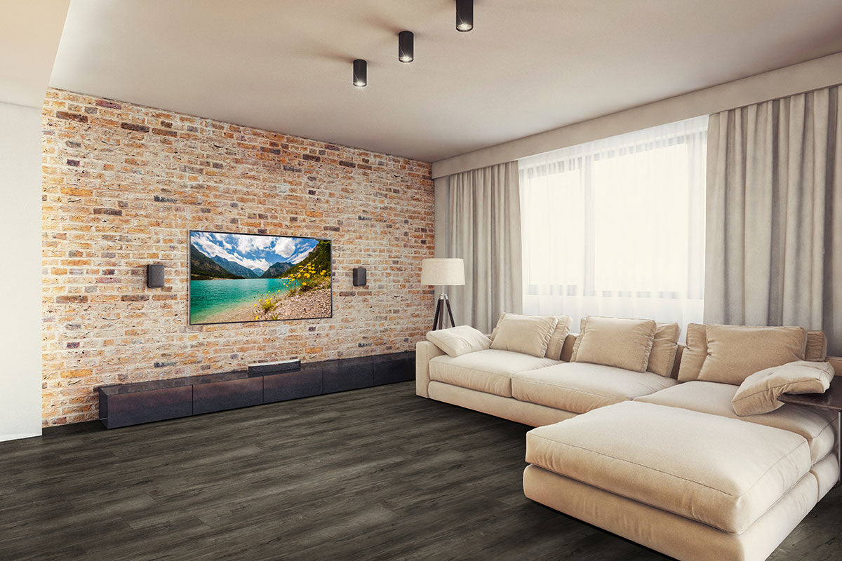 Modern living room with a beige sectional sofa, brick accent wall, mounted TV, floor lamp, large window with sheer curtains, and stylish MSI XL Cyrus Billingham Luxury Vinyl Planks featuring CrystaLux™ protection for lasting durability.