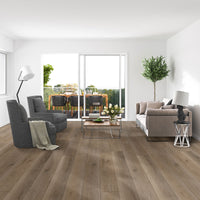Modern living room with MSI XL Cyrus Cranton Luxury Vinyl Planks flooring (22.44 SQFT/box), 100% waterproof, light wood look, gray armchairs, beige sofa, glass coffee table with flowers, potted plant; sliding doors open to green outdoor dining.
