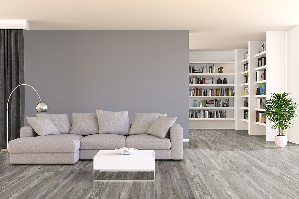 A modern living room with a gray sectional, light gray walls, white coffee table, floor lamp, bookshelves of books, potted plant, all on MSI XL Cyrus Draven Luxury Vinyl Planks—waterproof flooring with easy click-lock installation.