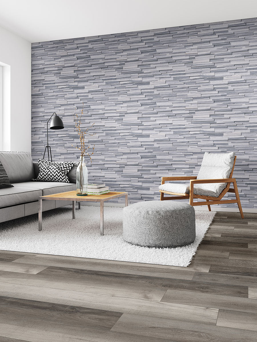 Modern living room with a grey textured accent wall, light grey sofa, wood armchair, ottoman, coffee table, black floor lamp, and white rug on MSI XL Cyrus Draven Luxury Vinyl Planks featuring a CrystaLux wear layer.